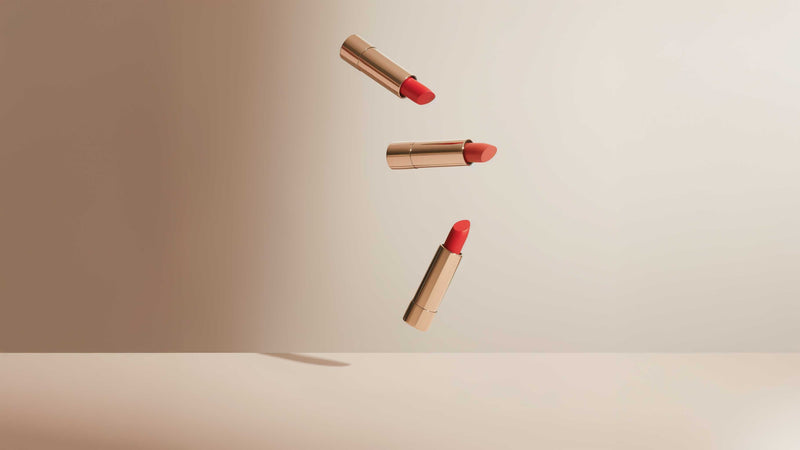 Rouge à lèvre bordeaux dans son étui noir et doré, posé sur une surface beige.
